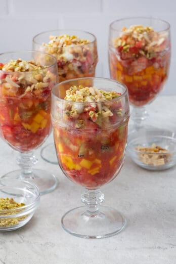 4 glasses of fruit cocktail, staggered, garnished with ashta on top and nuts sprinkled