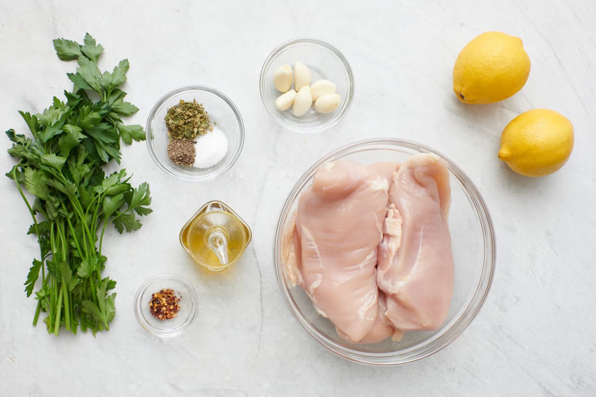 Ingredients for recipe: fresh parsley, spices, oil garlic cloves, chicken breasts, and whole lemons.