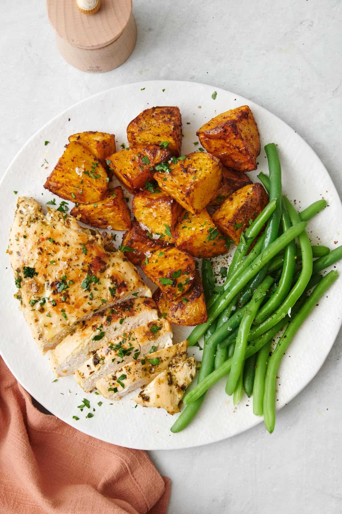Lemon garlic chicken on a plate with crispy potato cubes and green beans.