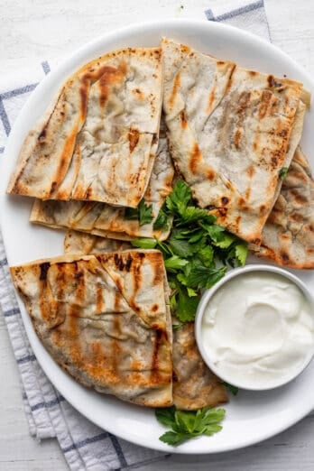 Lebanese meat stuffed pita triangles served on a white platter with a small bowl of yogurt and parsley for garnish