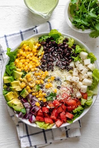 Mexican chopped salad in a large bowl with dressing on the side along with cilantro