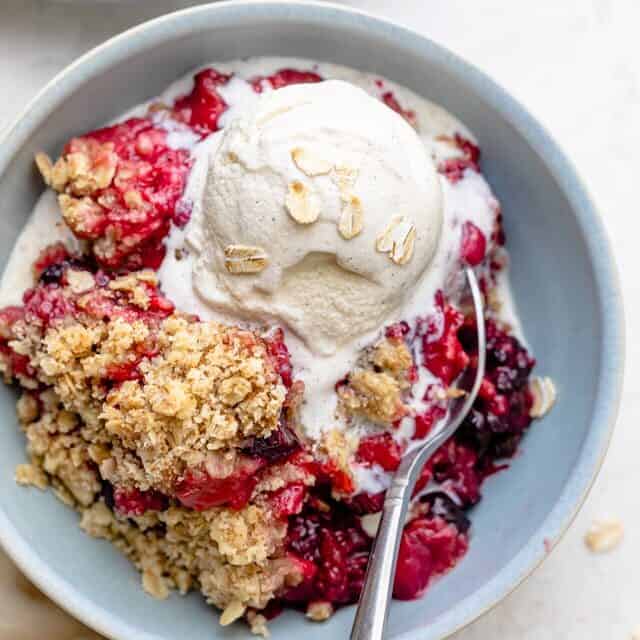 mixed berry crisp in a bowl with a scoop of ice cream