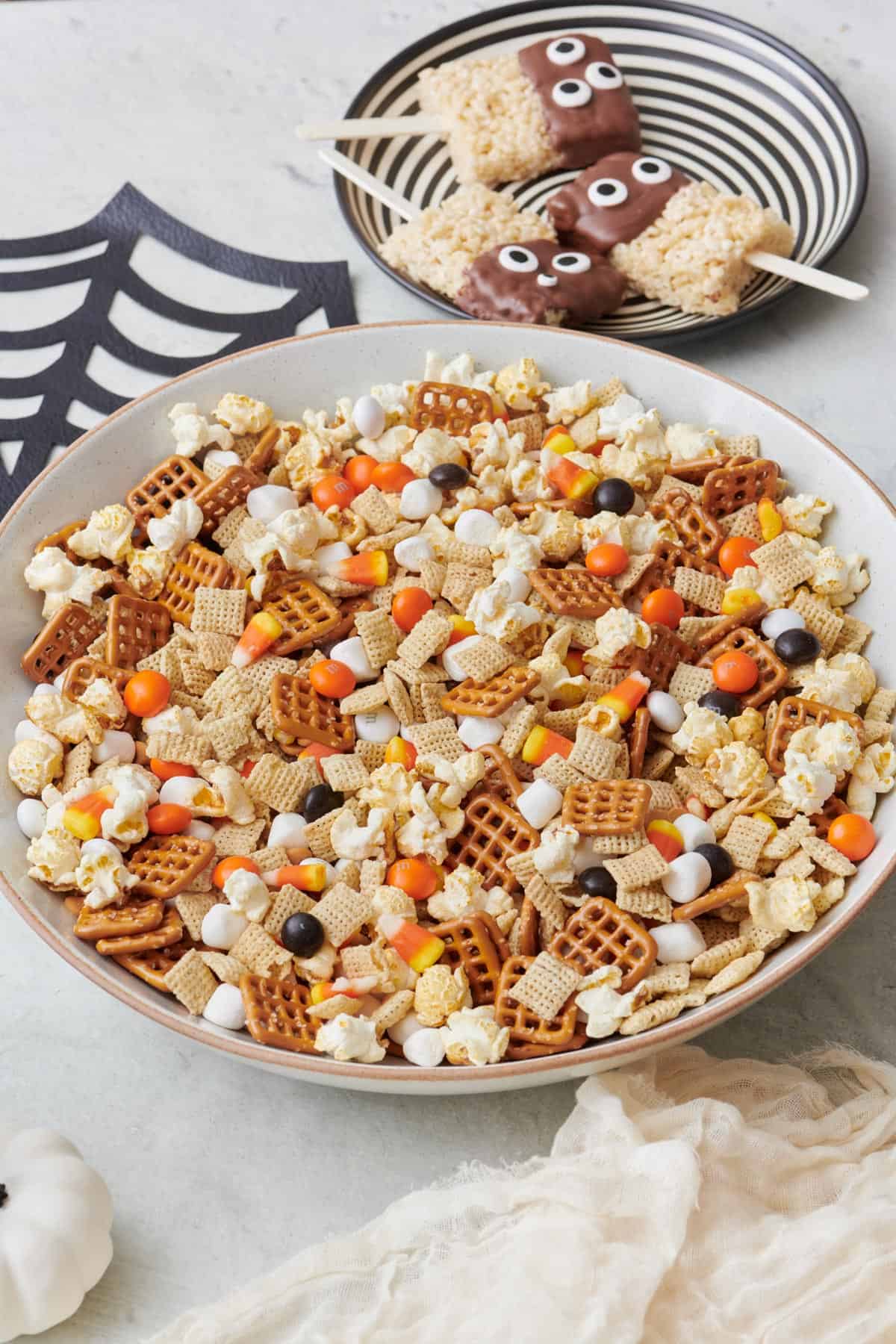 Monster munch trail mix with mini marshmallows, pretzels, popcorn and candy pieces in a bowl with monster rice krispies nearby.