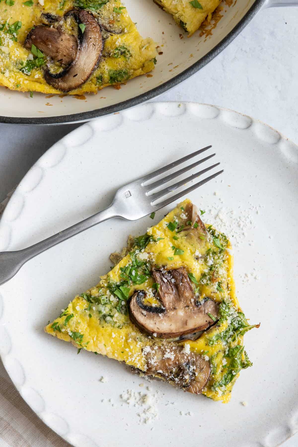 Slice of mushroom frittata served on a plate with fork and baking dish off to side.