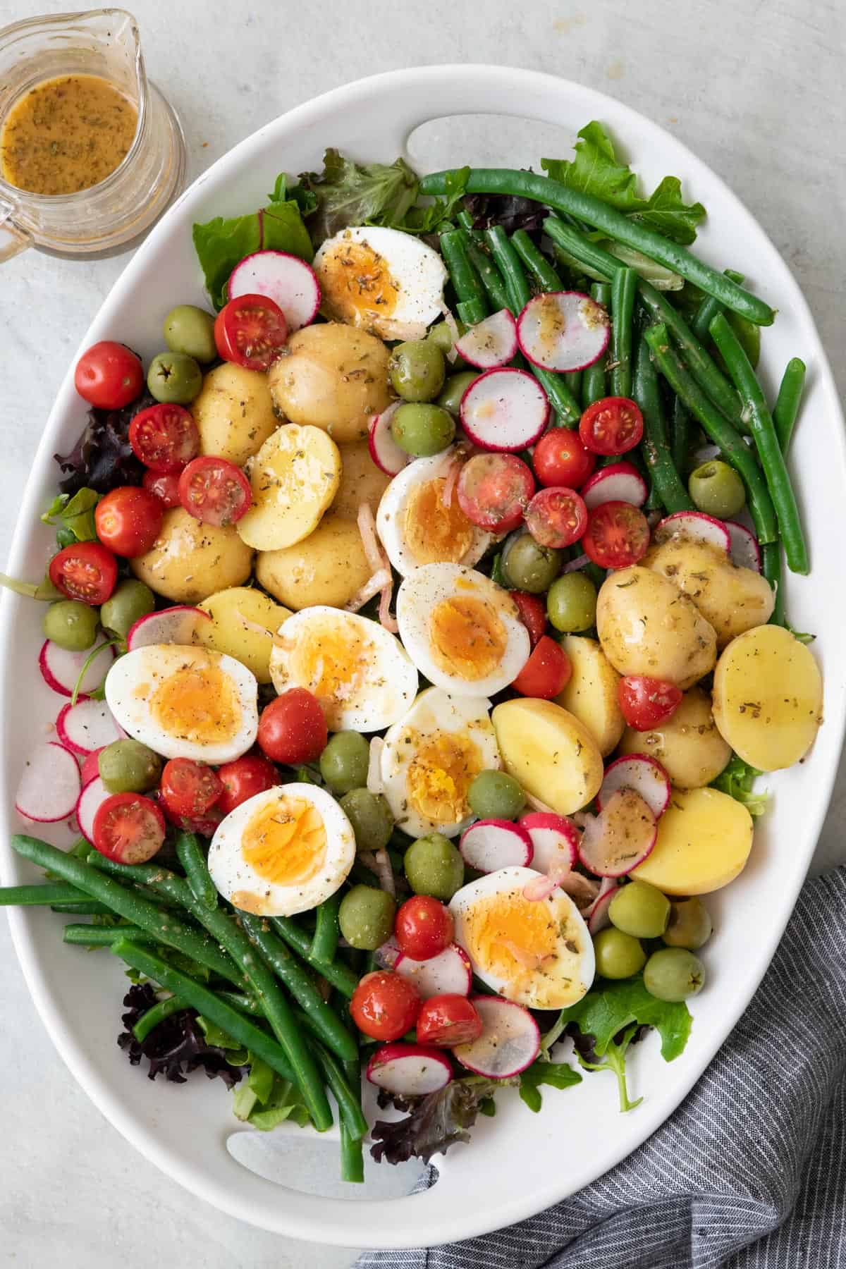 Nicoise salad on a large oval platter with dressing poured over and extra on the side.