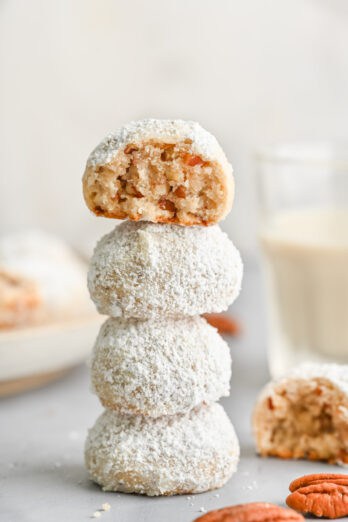 Four pecan snowball cookies stack on top of each other with the top cookie having a bite removed.