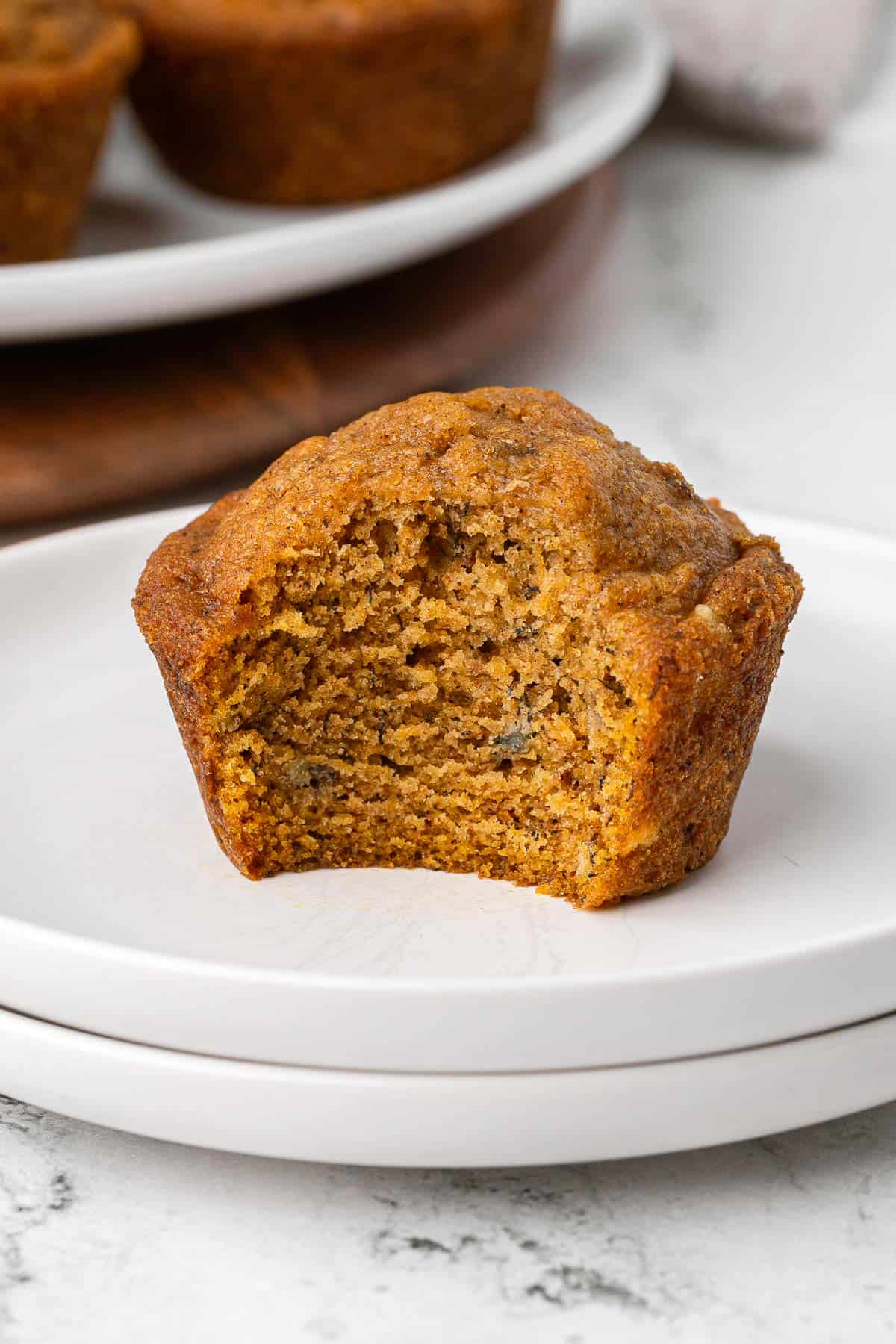 Pumpkin banana muffin on a small plate with a bite taken out to show inside texture.