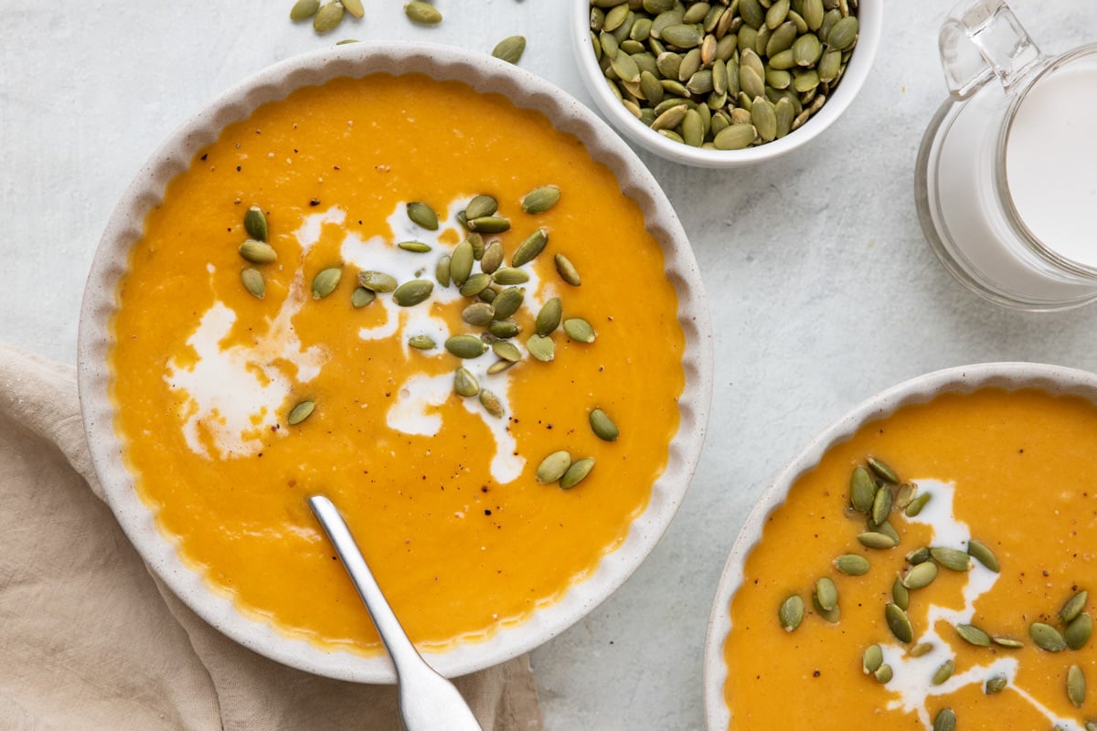 Two bowls of butternut squash soup with cream drizzled in and topped with pumpkin seeds.