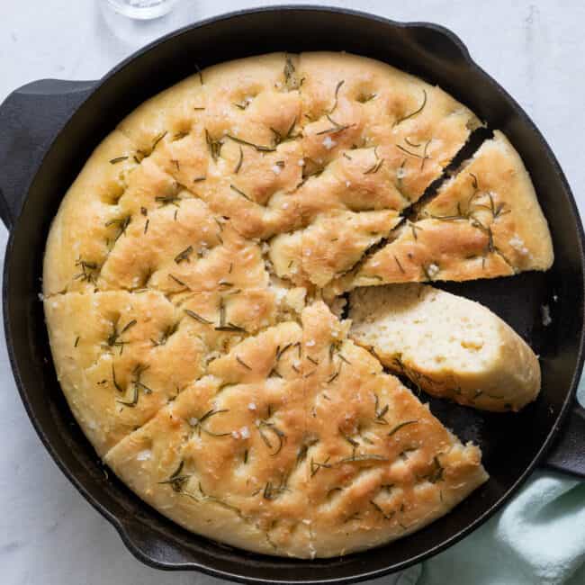 Focaccia in skillet cut into 8 slices with one slice flipped over to show texture.