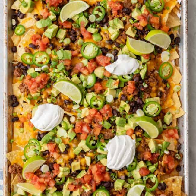 Hand lifting up a few chips from the Sheet Pan Nachos.