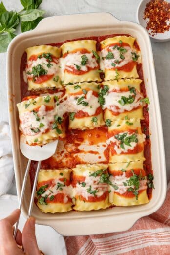 Baking dish of spinach lasagne roll ups garnished with fresh chopped basil and a spatual removing a piece.