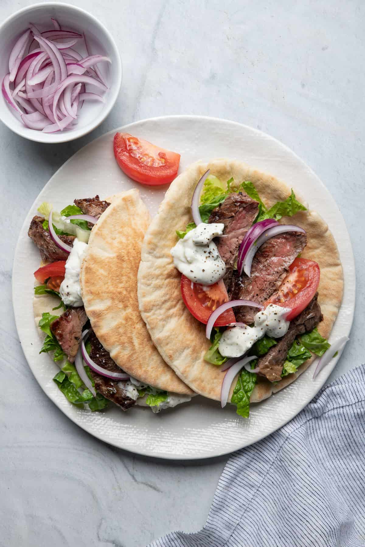 Two steak gyros on a plate with toppings
