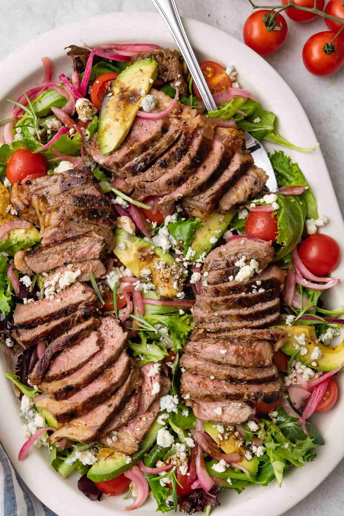 Spoon dipped into a large platter of steak salad.