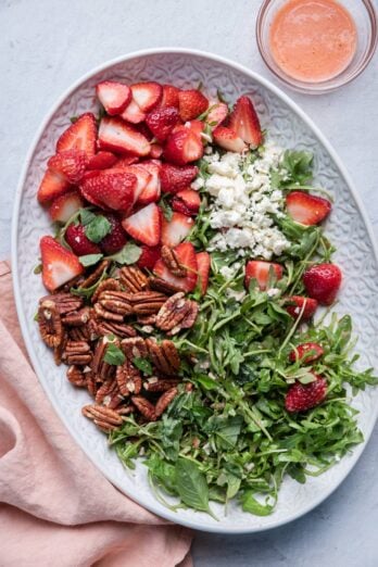 Strawberry Arugula Salad on a large platter with the dressing in a small bowl next to it