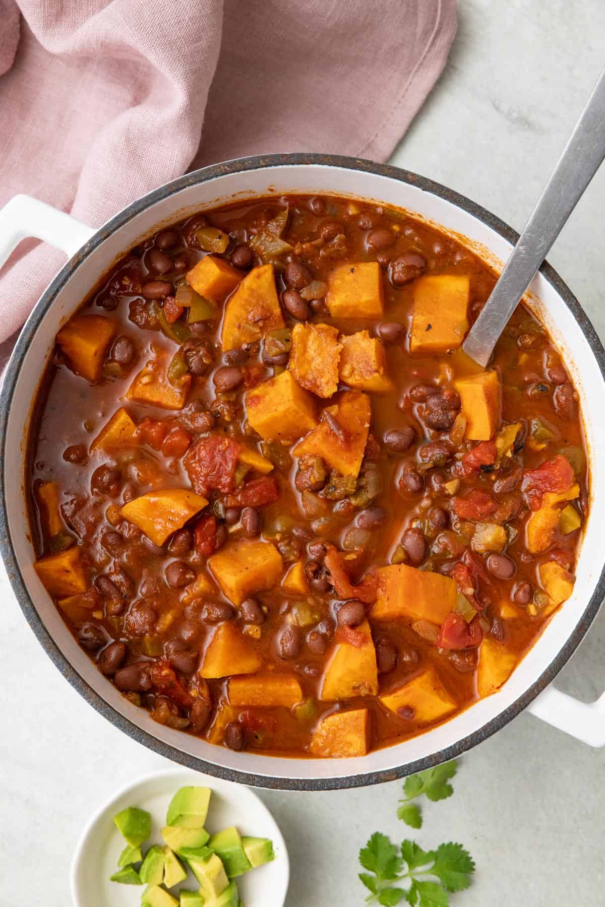 Sweet potato chili in pot with a ladle dipped inside. Small bowl of diced avocado nearby.