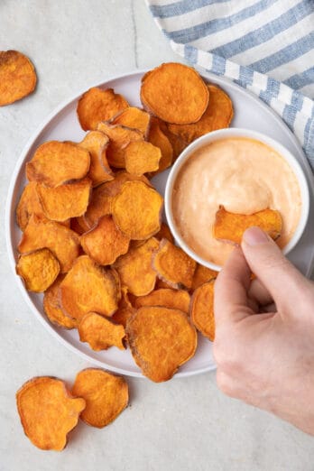Plate of sweet potato chips with one chip being dipped into spicy mayo.