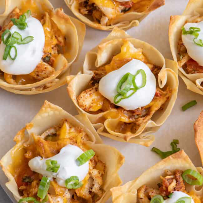 Close up of taco cups with chicken, cheese, sour cream and green onions.