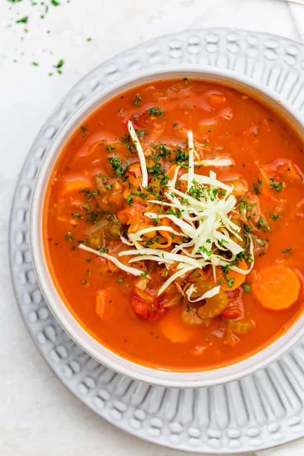 Tomato cabbage soup in a white bowl topped with fresh cabbage