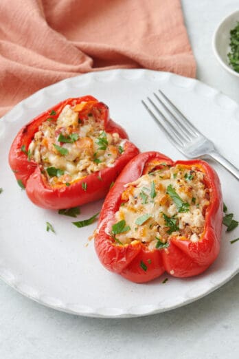 Two turkey stuffed peppers with melted cheese on top on a plate with a fork, garnished with fresh parsley.