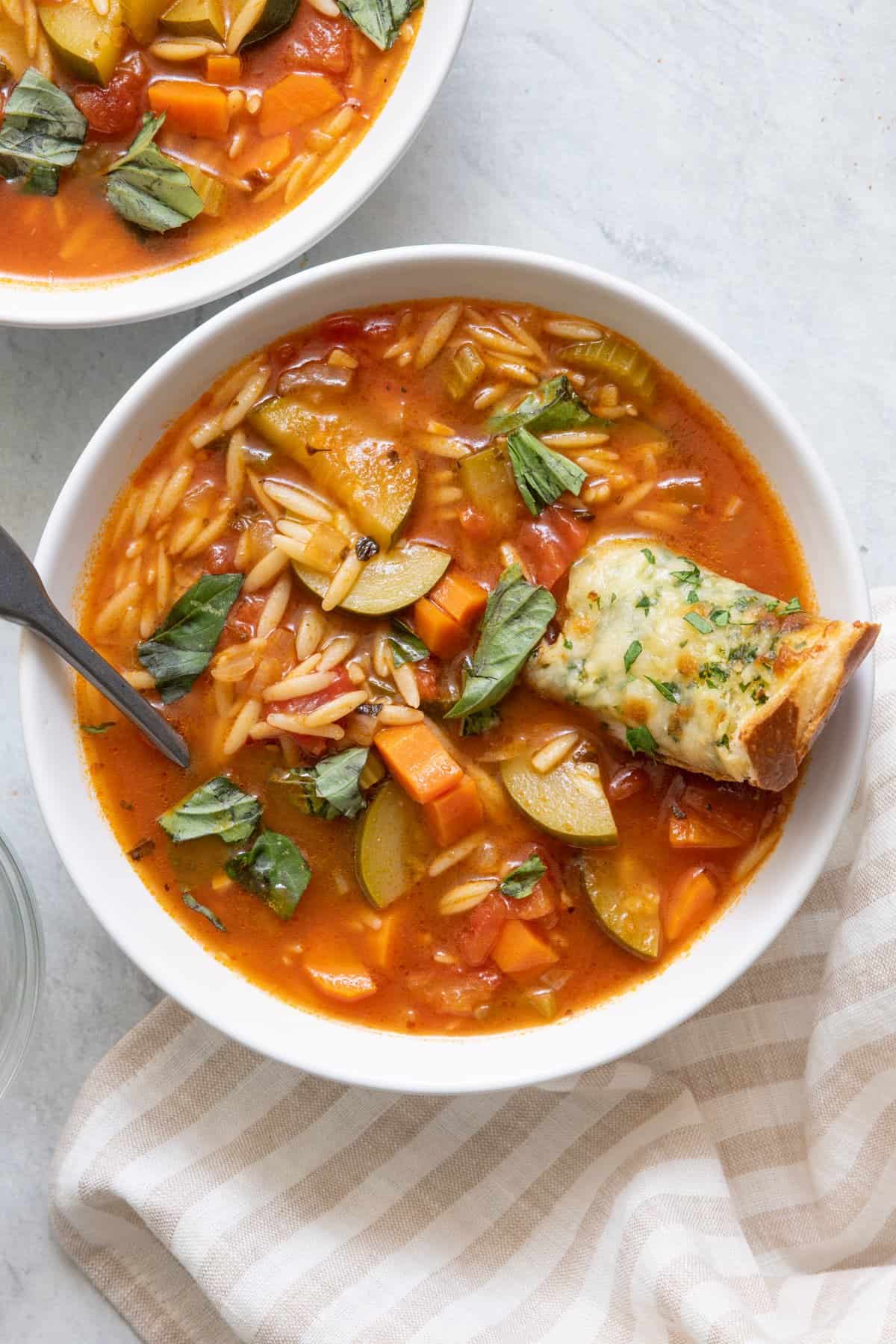 Bowl of zucchini orzo soup with a piece of cheese bread on top.